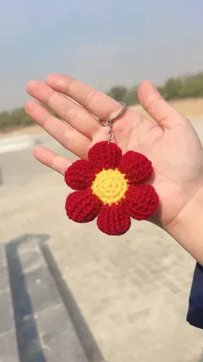 Red crochet flower keychain with a yellow centre held in a hand